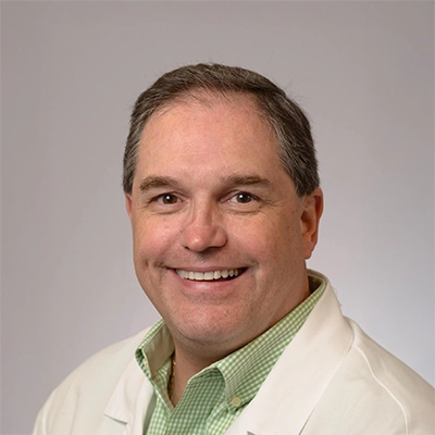 Orthodontist P. Todd Bonner In Lab Coat In Front Of Grey Background Smiling